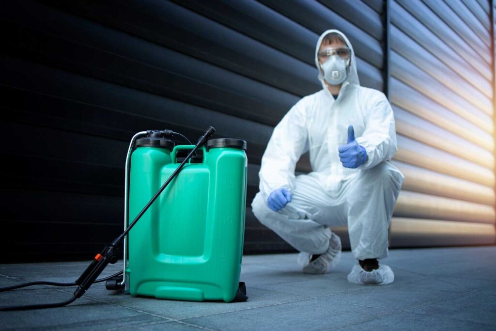 A farmer wearing Hazmat Suit, sitting with sprayer of Insecticides to be used over his crop